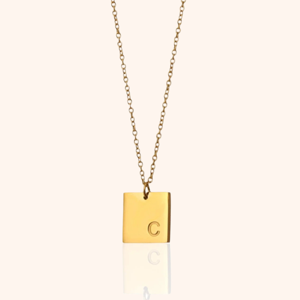 Close-up of a gold square pendant necklace with the initial "C" engraved, showcasing its personalized design.